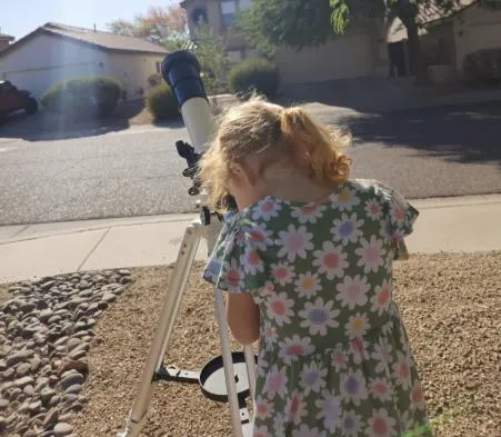 A young child looking through a telescope eyepiece in her front yard